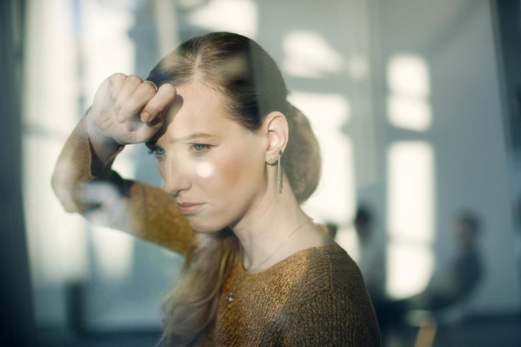 young sad woman leaning window looking through it min